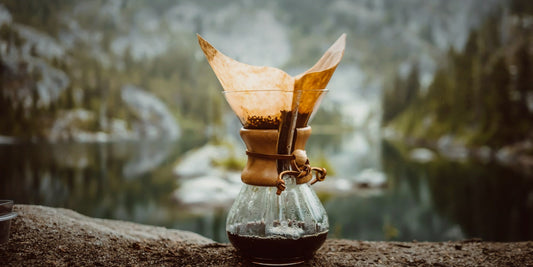 A Chemex coffee brewer beside a mountain lake