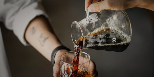 Dark coffee being poured over ice into a glass, lit dramatically against a dark background