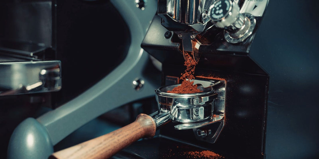 Ground coffee dosed into a bottomless portafilter basket on a dark machine