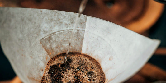 Water poured onto a coffee bed in a white paper filter cone, lit low