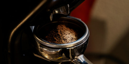 A burr grinder dosing fresh grounds into a portafilter, lit low against a dark background