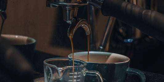 An espresso machine group head pulling a dark shot into a glass, lit low