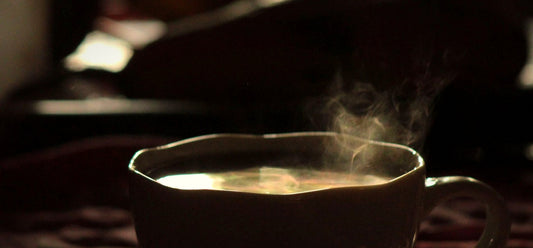 A dark cup of coffee with steam rising over a moody table