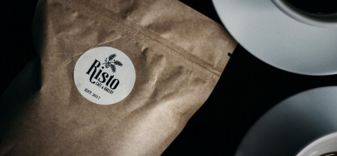 A dark coffee bag with a round paper label beside a cup