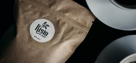 A dark coffee bag with a round paper label beside a cup