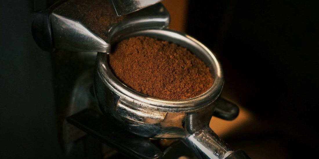 A portafilter of freshly ground coffee coming off a grinder, lit against a dark background