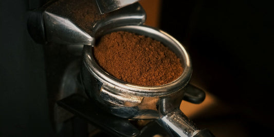 A portafilter of freshly ground coffee coming off a grinder, lit against a dark background