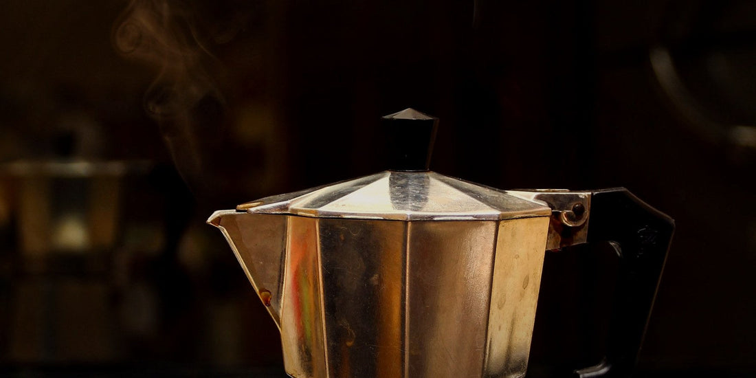A moka pot steaming on a stove, lit warmly against a dark background