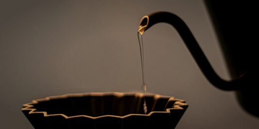A gooseneck kettle pouring water into a dark coffee dripper, lit dramatically